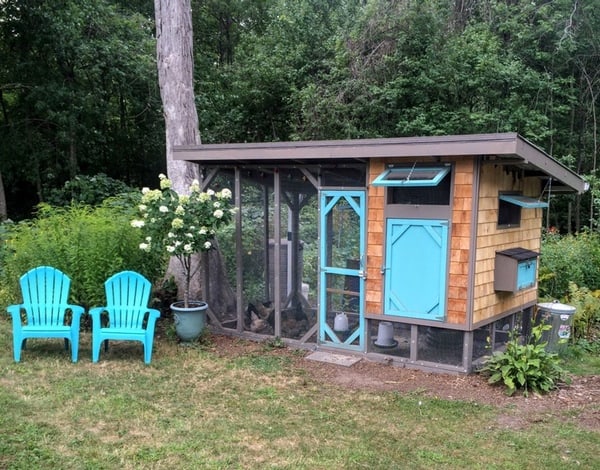 A small chicken coop with two chairs in front.
