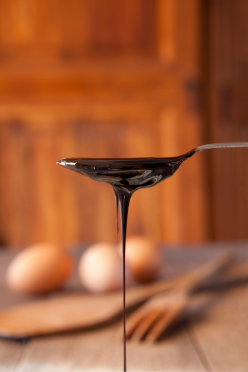 Molasses dripping off a spoon, eggs and utensils in the background. 