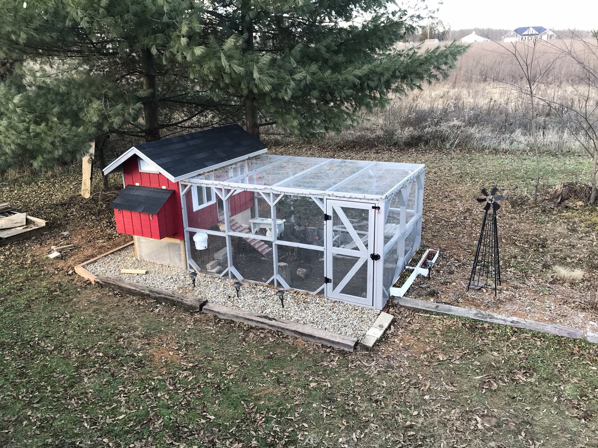 elevated chicken coop with large enclosed run and red nesting box in backyard setting